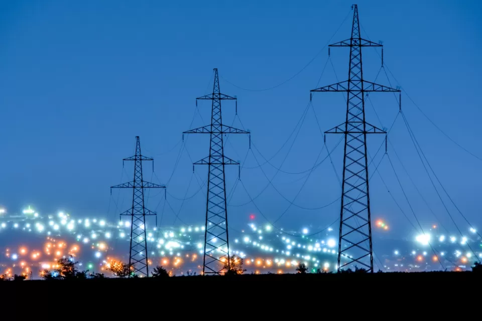 Tall power line towers with blurred city lights in background.